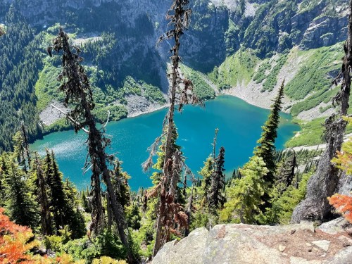 Aerial view of a vibrant blue lake surrounded by lush green mountains and tall evergreen trees.