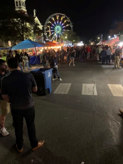 A lively night market scene with crowds, food stalls, and a colorful Ferris wheel in the background.