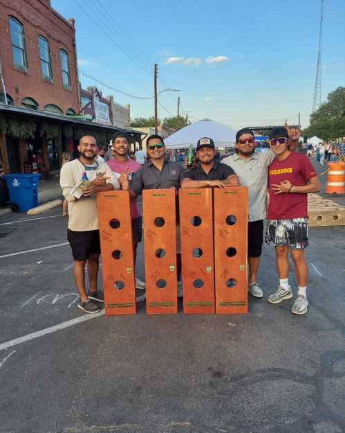 A group of six people poses with large wooden blocks at an outdoor event, smiling and enjoying the day.