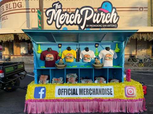 A colorful merchandise booth displaying T-shirts and hats, with social media logos and "Official Merchandise" sign.