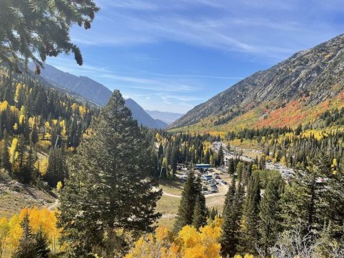 A scenic view of a valley surrounded by mountains, featuring vibrant autumn foliage and a parking area below.