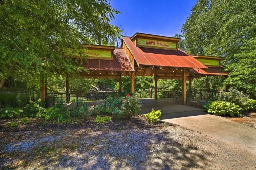 Entrance to a nature-themed venue with a wooden structure, red roof, and lush greenery surrounding the pathway.