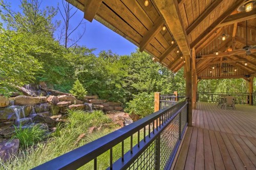 A wooden deck with a view of a lush green landscape and a small waterfall, under a bright blue sky.