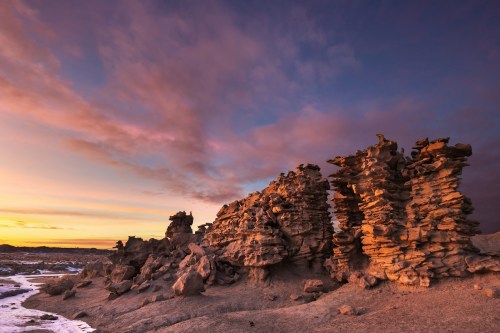 Rock formations at sunset, with layered stones illuminated by warm light against a colorful sky.