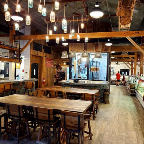 A rustic dining area with wooden tables, hanging lights, and a display counter in a cozy, inviting atmosphere.