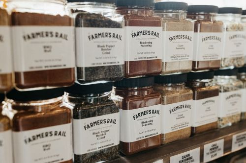 A row of spice jars labeled "Farmer's Rail," featuring various spices and seasonings on a wooden shelf.