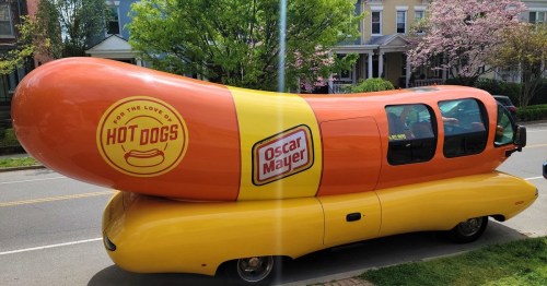 A colorful Oscar Mayer Wienermobile parked on a street, resembling a giant hot dog on a bun.