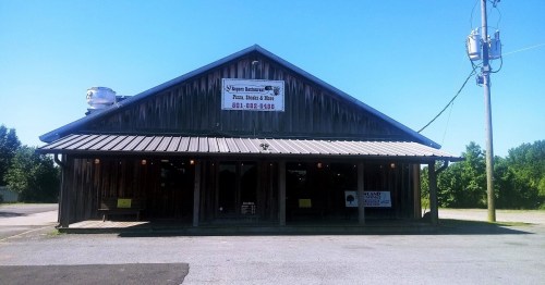 A rustic wooden building with a metal roof, featuring a sign for a restaurant and a clear blue sky above.