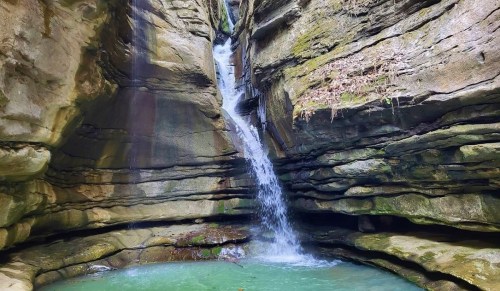 A serene waterfall cascading into a turquoise pool, surrounded by rugged rock formations and lush greenery.