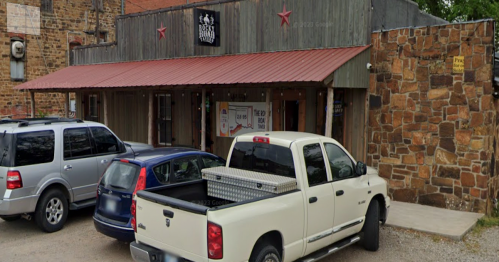 A rustic building with a wooden facade and red roof, featuring parked cars in front and a sign on the wall.