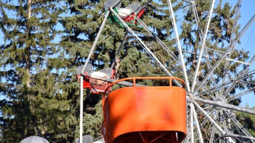 A colorful ferris wheel with red and orange seats against a backdrop of green trees.