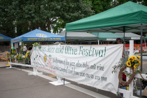 A banner for the Jazz and Olive Festival, with tents and decorations in a park setting.