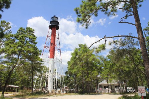 A tall red and white lighthouse surrounded by trees under a blue sky with clouds.