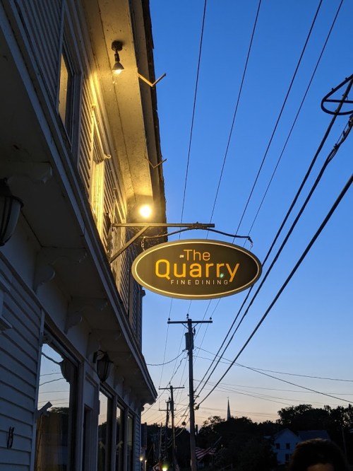 Sign for "The Quarry Fine Dining" illuminated at dusk, with power lines and a clear blue sky in the background.