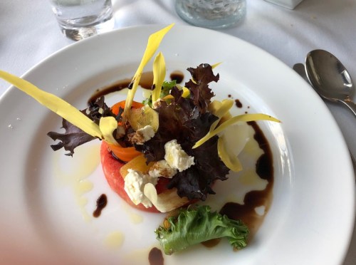 A colorful salad with mixed greens, sliced vegetables, and drizzled dressing on a white plate.