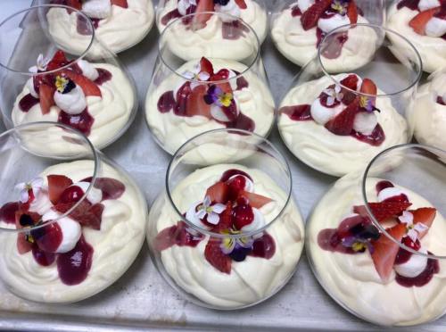 A tray of elegant dessert cups filled with creamy mousse, topped with strawberries, cherries, and edible flowers.
