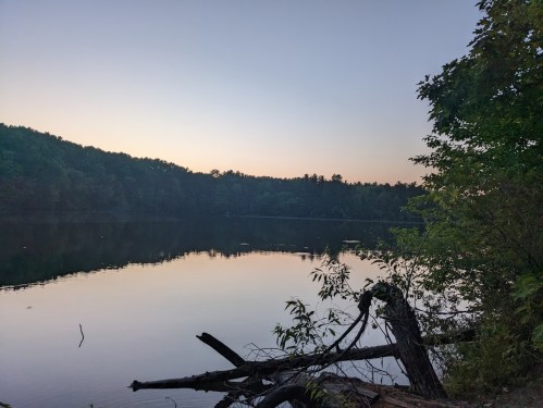 A serene lake at dusk, surrounded by trees and reflecting the soft colors of the sky.
