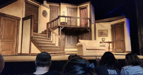 A theater stage set featuring a staircase, doors, a couch, and a small table, ready for a performance.