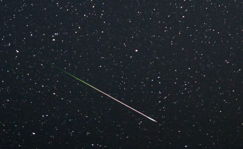 A bright meteor streaks across a starry night sky, leaving a colorful trail against the dark backdrop.