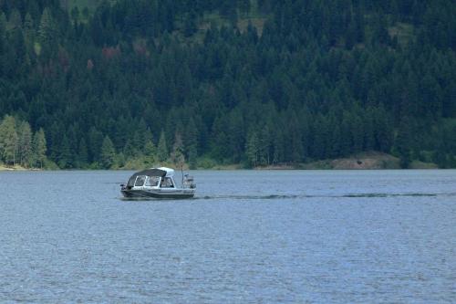 A small boat glides across a calm lake, surrounded by lush green forests and distant hills.