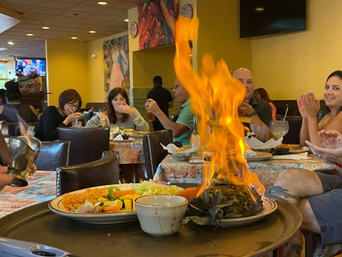 A vibrant restaurant scene with a flaming dish on a table, surrounded by diners enjoying their meals.
