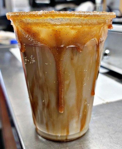 A clear cup filled with iced coffee, topped with caramel sauce dripping down the sides.
