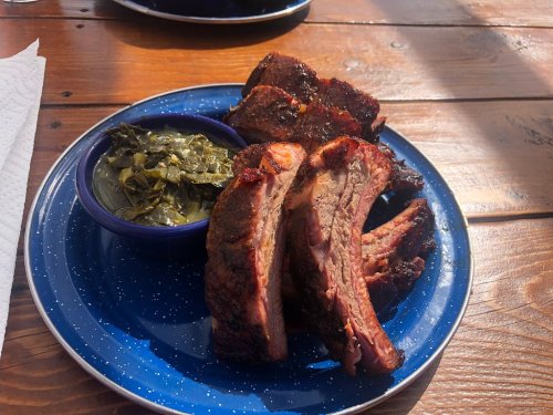 A blue plate with smoked ribs and a side of collard greens on a wooden table.