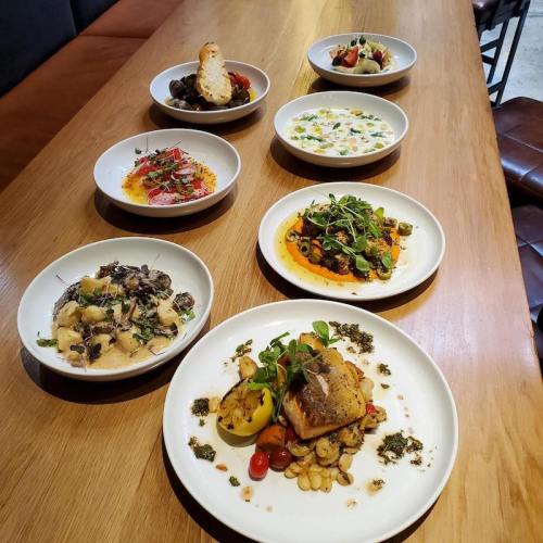 A wooden table with eight plates of various gourmet dishes, including seafood, pasta, and colorful salads.