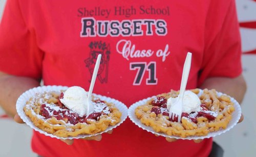 Two plates of funnel cakes topped with cherry filling and ice cream, held by a person wearing a red Shelley High School shirt.