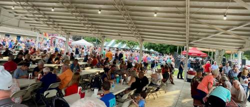 A crowded outdoor event under a large tent, with people seated at tables and enjoying the festivities.