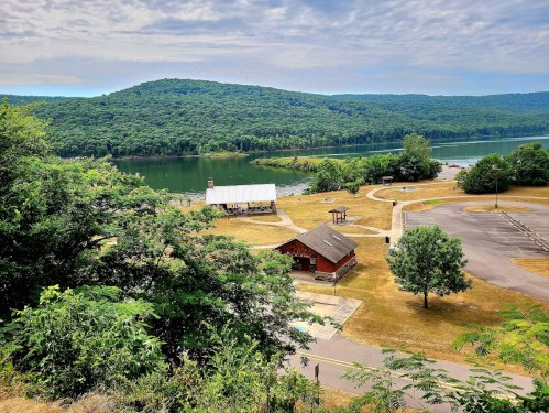 Scenic view of a lake surrounded by green hills, with a picnic area and parking lot in the foreground.