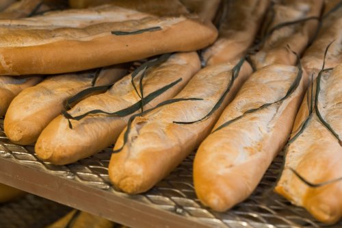 Freshly baked baguettes with green herbs resting on a wire rack.