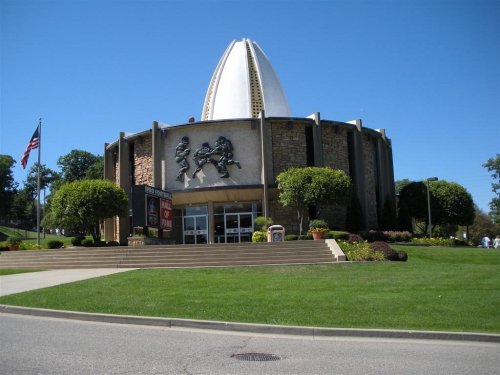 Exterior view of a unique building with a dome, featuring stone walls and sculptures, surrounded by green grass and trees.