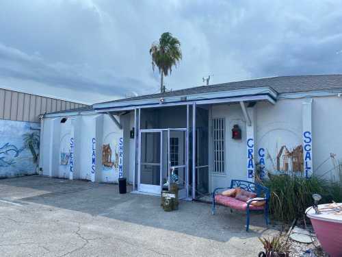 A seafood restaurant entrance with blue accents, featuring signs for steak, shrimp, crab, and scallops, under a cloudy sky.