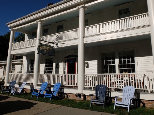 A charming inn with a sign, featuring a porch and several colorful adirondack chairs in front.