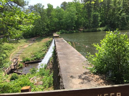 A serene landscape featuring a stone dam, flowing water, and lush greenery surrounding a calm lake.