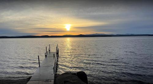 A serene lake at sunset, with a wooden dock extending into the water and mountains in the distance.