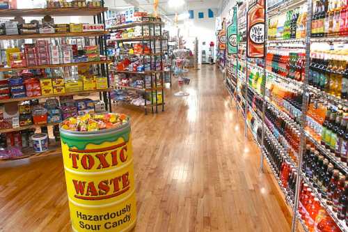 A colorful candy store aisle with shelves of snacks and drinks, featuring a prominent "Toxic Waste" candy barrel.