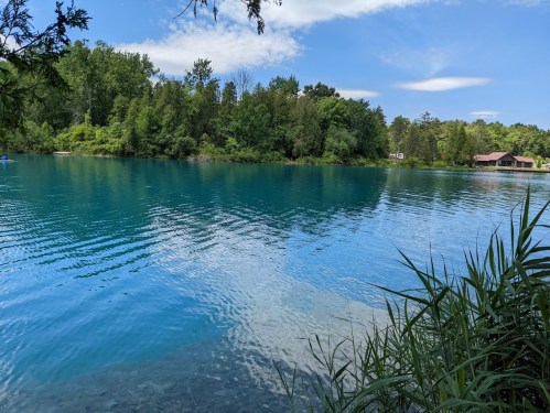 A serene lake surrounded by lush greenery under a clear blue sky, with gentle ripples on the water's surface.