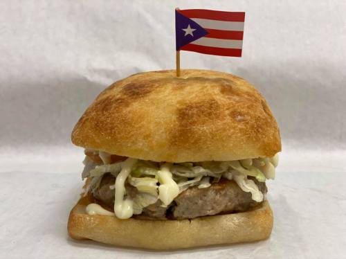 A sandwich with a meat patty, lettuce, and mayonnaise, topped with a small Puerto Rican flag.