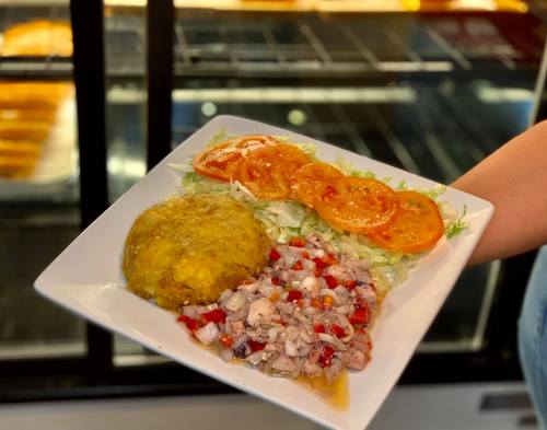 A plate with yellow rice, fresh salad, sliced tomatoes, and a seafood ceviche mix.