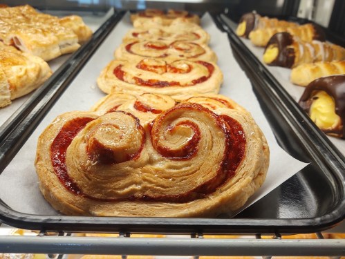Freshly baked pastries with a swirl design, featuring a glossy red filling, displayed in a bakery case.
