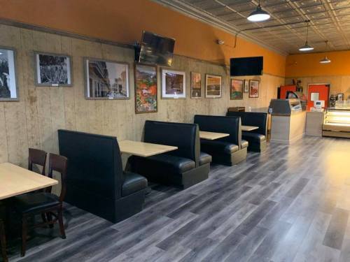 Interior of a cozy restaurant featuring wooden walls, black booths, and framed artwork, with a display case in the background.