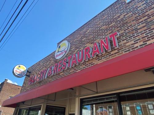 Signage of a bakery and restaurant with a red awning, featuring the name "Gualy" on a brick building.
