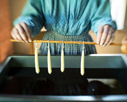 A person in a blue shirt hangs four candles on a wooden stick above a dark container.