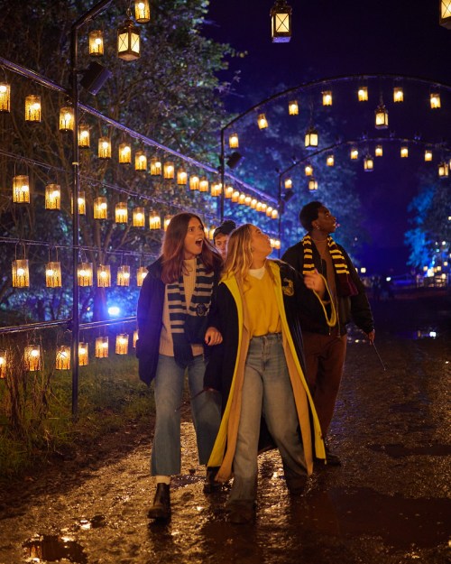 A group of friends walks along a lantern-lit path at night, wearing casual clothes and enjoying the festive atmosphere.
