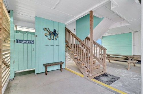 A light blue outdoor area featuring a shower, wooden stairs, and a picnic table under a covered space.