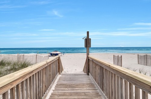 A wooden boardwalk leads to a sandy beach and calm ocean under a clear blue sky.