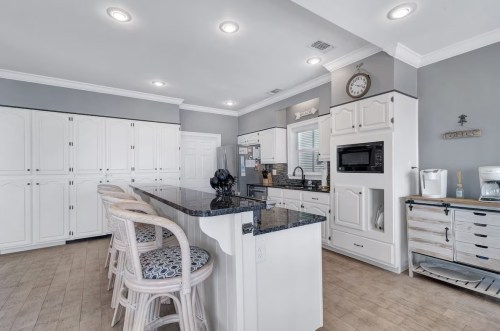 Modern kitchen with white cabinets, granite island, bar stools, and stainless steel appliances in a bright, open layout.
