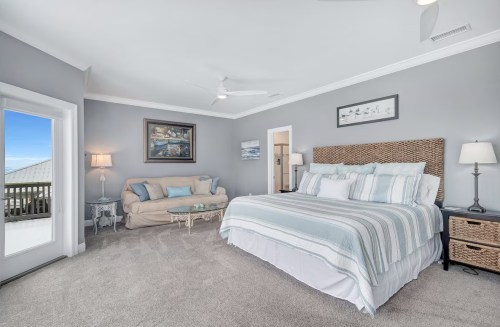 Spacious bedroom with a large bed, cozy sofa, and light gray walls, featuring a balcony door and decorative artwork.